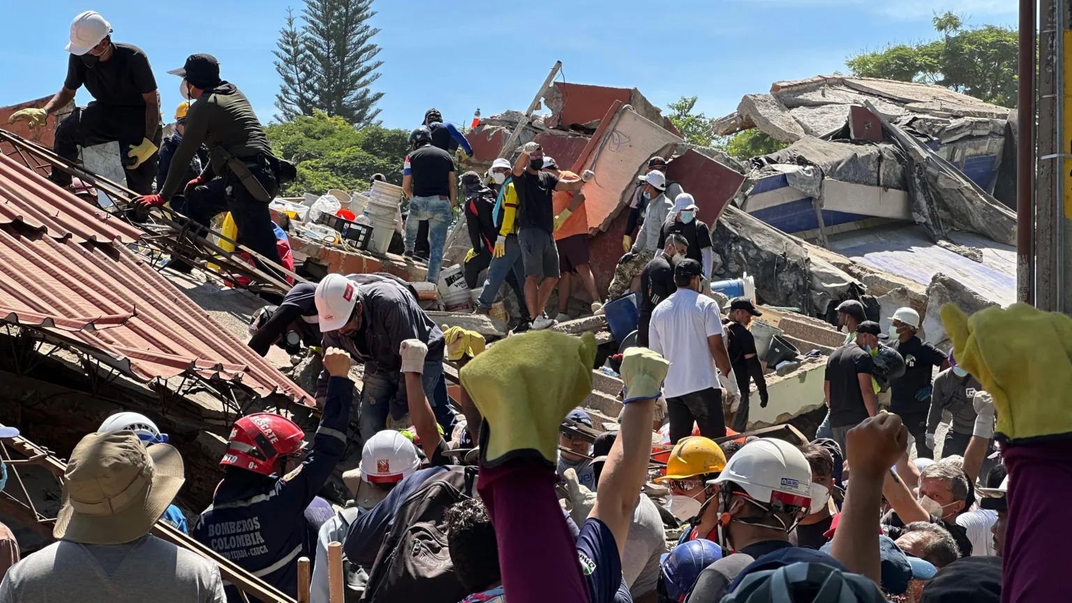 (Para pekerja dan relawan mengangkat tangan ke udara sebagai simbol agar suasana menjadi tenang, demi memungkinkan suara penyintas terdengar. (Foto: BBC News))